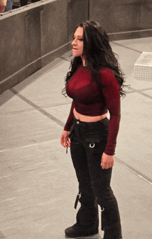 a woman in a red top and black pants is standing on a concrete floor