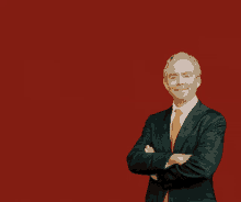 a man in a suit and orange tie stands with his arms crossed in front of a red background