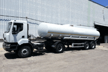 a white truck with a large tank on the back is parked in front of a building