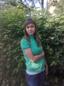 a woman in a green sweater stands in front of a bush