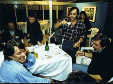 a group of men are sitting at a table with a bottle of wine on it