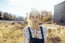 a woman in overalls stands in a field with a barn in the background