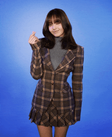 a woman in a plaid jacket and skirt is making a heart shape with her hand