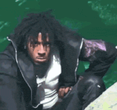 a man in a black jacket is sitting on a rock near a body of water