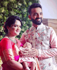 a man and a woman are holding a baby and smiling for the camera .