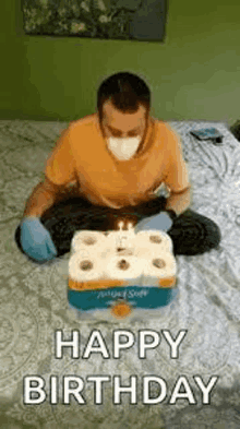 a man wearing a mask and gloves is sitting on a bed with toilet paper rolls and a birthday cake .