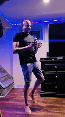 a man in a black shirt and blue shorts is holding a can of beer