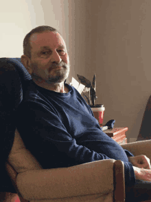 a man in a blue shirt sits in a chair in front of a plant