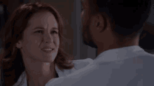 a man and a woman are looking at each other in a room . the woman is wearing a lab coat .