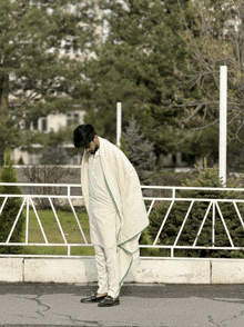 a man in a white blanket stands in front of a fence with the letter z on it