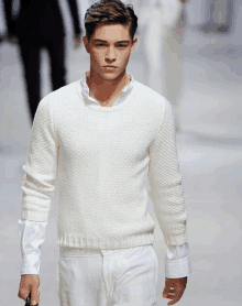 a young man wearing a white sweater and white pants walks down the runway