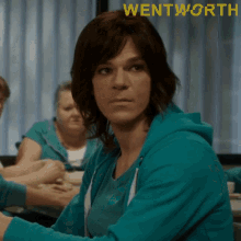 a woman in a blue sweatshirt is sitting at a table with the word wentworth on the bottom right