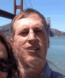 a man and woman are posing for a picture in front of a bridge .