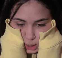 a young woman wearing a yellow sweater is making a funny face with her tongue out .