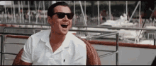 a man wearing sunglasses is laughing while sitting in a chair on a boat .