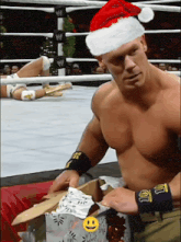 a shirtless wrestler wearing a santa hat is opening a gift box