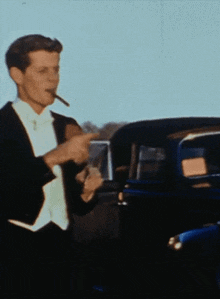 a man in a tuxedo is smoking a cigarette in front of a car