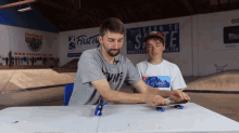 a man and a boy are sitting at a table in front of a sign that says first to skate