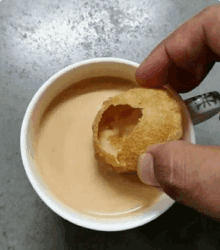 a person is dipping a fried food in a cup of coffee .