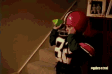 a young boy dressed as a football player is drinking water from a bottle while standing on a set of stairs .