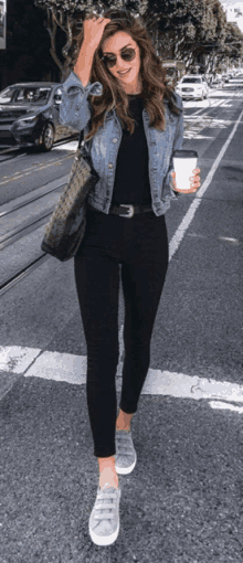 a woman wearing a denim jacket and black pants is walking down the street .