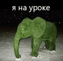 a green elephant statue is standing in the snow at night .