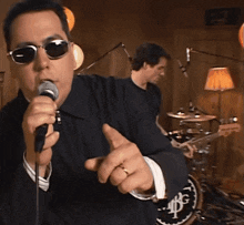 a man wearing sunglasses is singing into a microphone in front of a drum set that has the letters bg on it