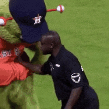 a mascot wearing a hat with the letter h on it kisses a referee