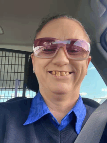 a woman wearing sunglasses and a blue shirt is smiling in a car