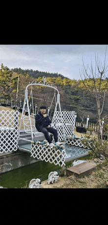 a man sits on a swing overlooking a body of water