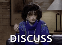 a woman in a blue sweater is sitting on a couch with the word discuss written on the screen .