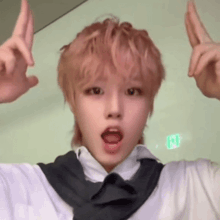 a young man with pink hair is making a funny face while making a peace sign with his hands .