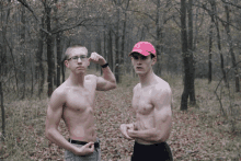 a shirtless man flexes his muscles next to a shirtless man wearing a red hat