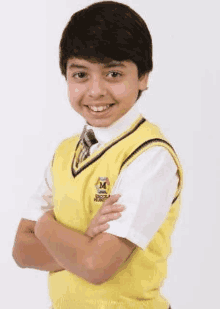 a young boy wearing a yellow vest and tie with his arms crossed is smiling .