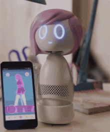 a robot with purple hair is standing next to a cell phone that shows a girl dancing