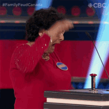 a woman in a red dress is standing in front of a podium with a button that says family feud canada