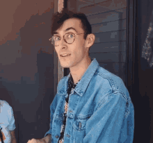 a man wearing glasses and a denim jacket is smiling