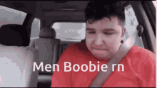 a man in a red shirt is sitting in the back seat of a car with the words men boobie rn on the screen .