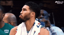 a basketball player with a towel around his neck sits in the stands at a boston game