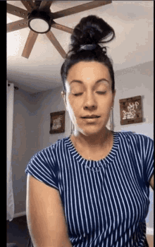 a woman in a blue and white striped shirt is standing in front of a ceiling fan in a living room .