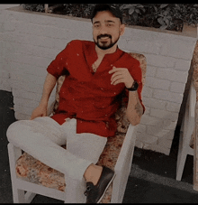 a man in a red shirt sits in a chair with his legs crossed