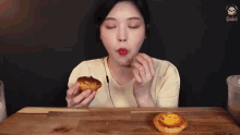 a woman is sitting at a table eating two pastries with her eyes closed