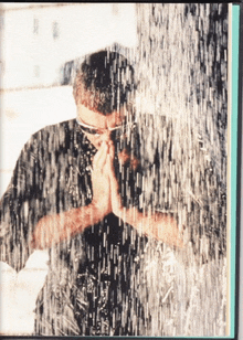 a man is standing in the rain with his hands folded in front of his face