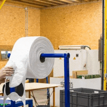 a person is holding a large roll of plastic wrap in a factory .