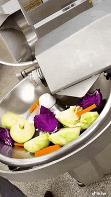 a stainless steel bowl filled with vegetables including apples and cabbage