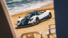 a black and white sports car is parked on the beach near the ocean