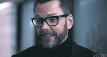 a man with glasses and a beard is smiling and the word decider is on the bottom right