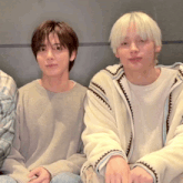 two young men sitting next to each other wearing sweaters