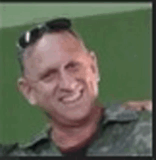 a man in a military uniform and sunglasses is smiling for the camera .