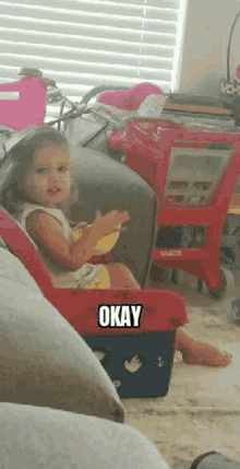 a little girl is sitting on a couch and making a funny face while holding a bowl of food .